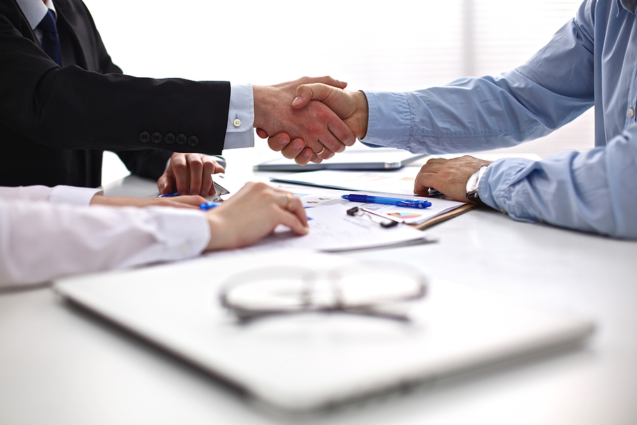 Two professionals shaking hands over a business meeting desk.